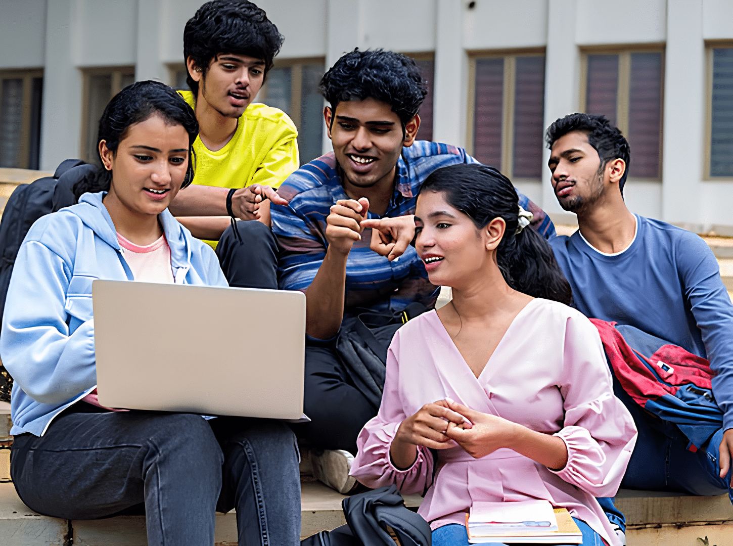 Students checking a laptop for documents required for study abroad while sitting together on campus steps.